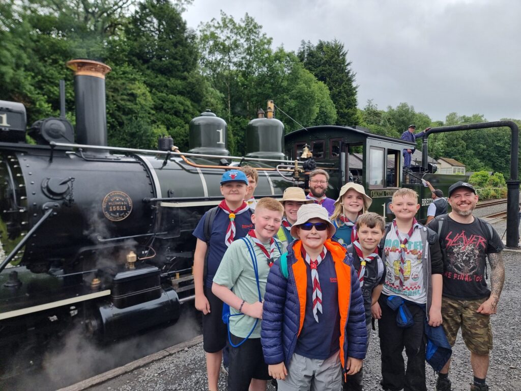 A group of Scouts and an adult volunteer standing in front of an old steam engine.